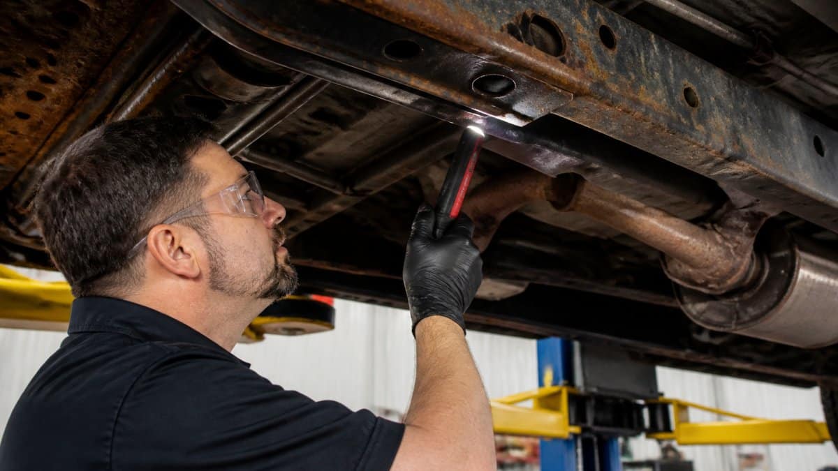 Mechanic using a flashlight to inspect a truck undercarriage to prevent rust on trucks